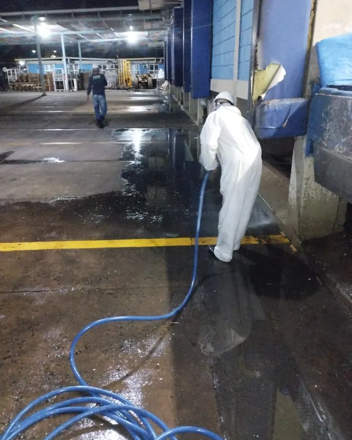 Profissional de macacão de proteção lavando piso de área industrial com mangueira