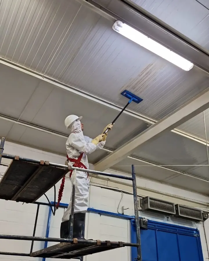 Profissional com macacão, capacete e cinto de segurança fazendo sanitização no forro de um galpão